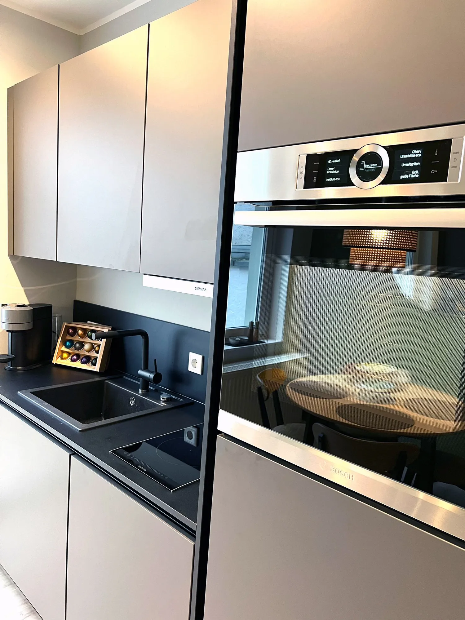 Graue Wohnküche mit Essplatz, Sofa und Backofen – Referenz von SORI Studios